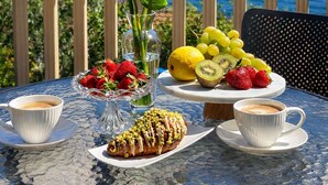 A table with a view of a lake and mountains, a vase with white flowers, a fruit bowl, and pastries. - Apartments Stella del Mare (Risan)