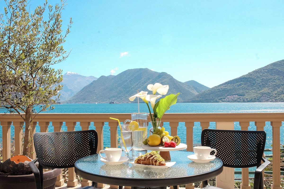 Une table avec une carafe, une tasse et une assiette de nourriture, donnant sur un lac bordé de montagnes.