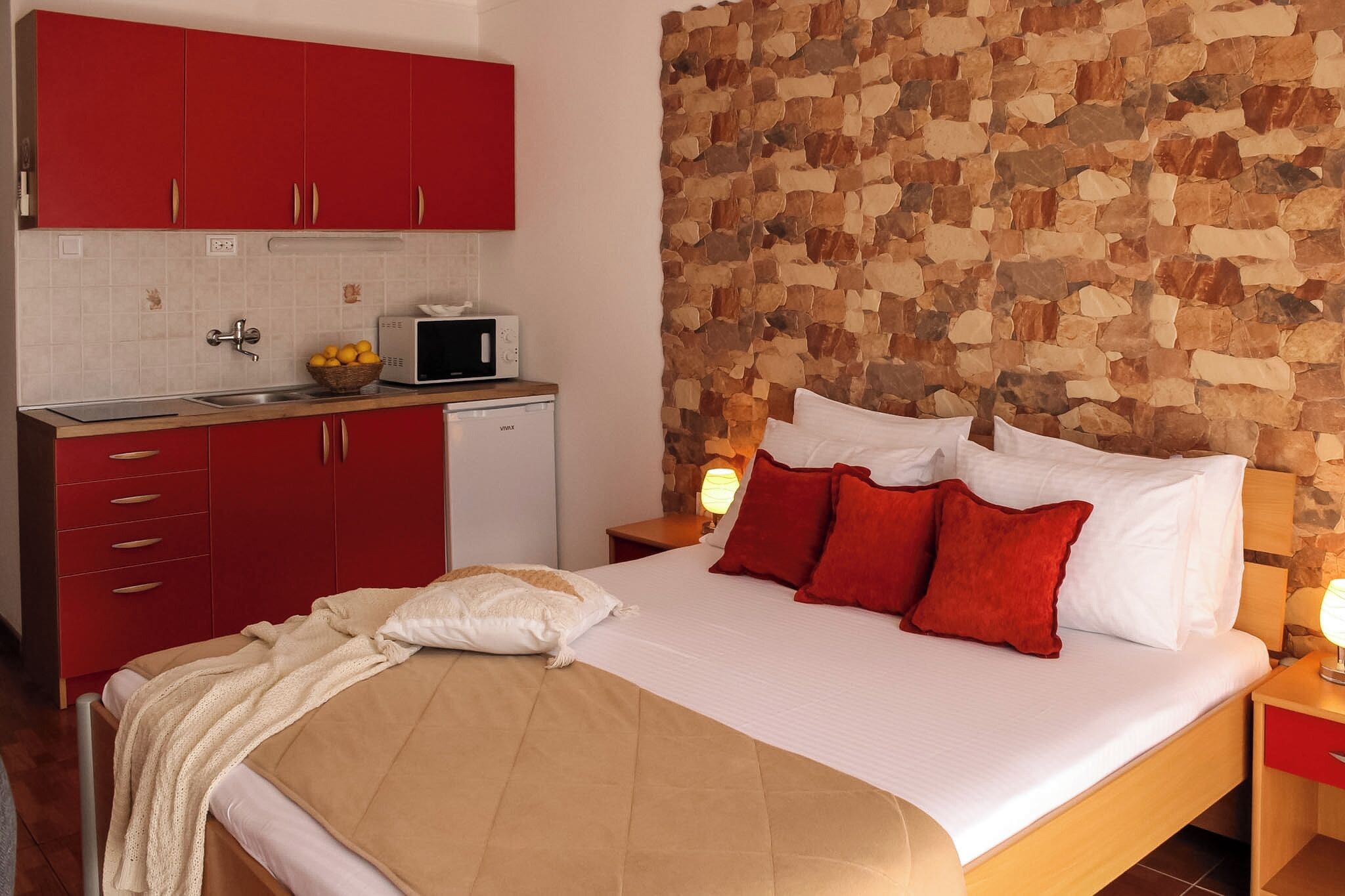 Een slaapkamer met een bed, rode kasten, een stenen muur, een magnetron en een wastafel.