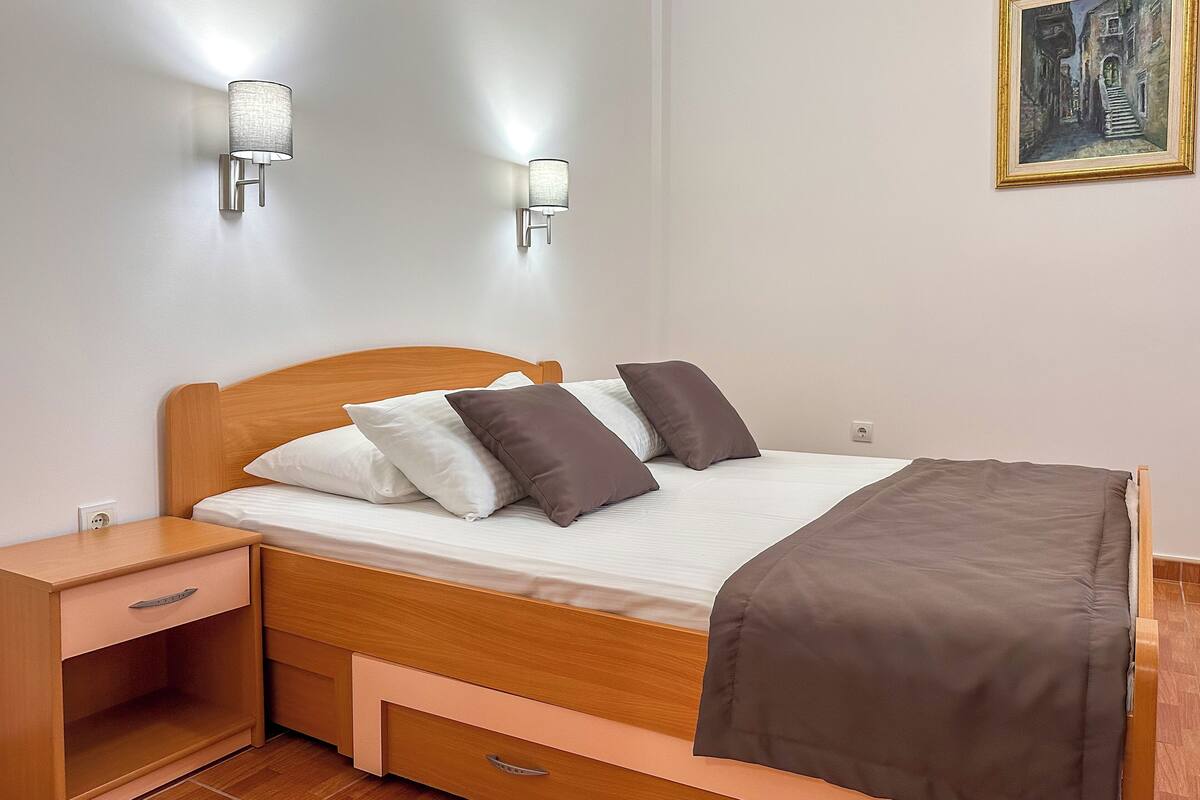 Un lit bien fait, avec une tête de lit en bois, deux tables de chevet, une commode et un tableau accroché au mur.