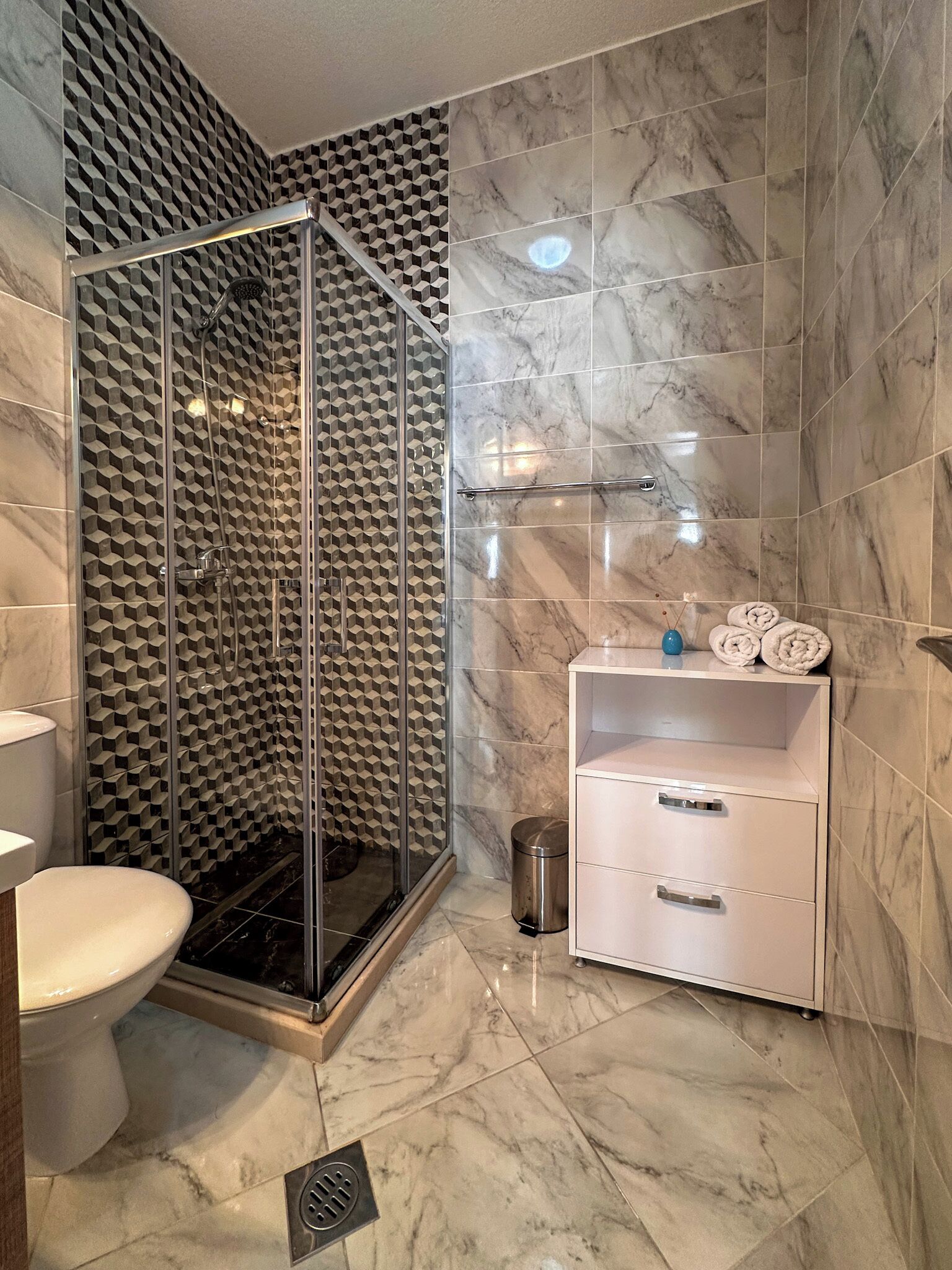 Een badkamer met douchecabine, toilet, wastafel en opslagruimte.
