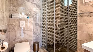A bathroom with a glass-enclosed shower, marble tiles, a toilet, and a towel rack.