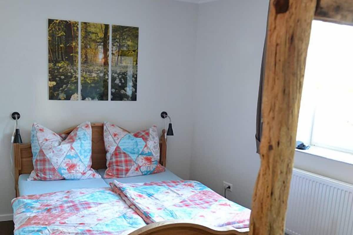 A bedroom with a wooden bed, floral bedding, and a window with a view of trees.