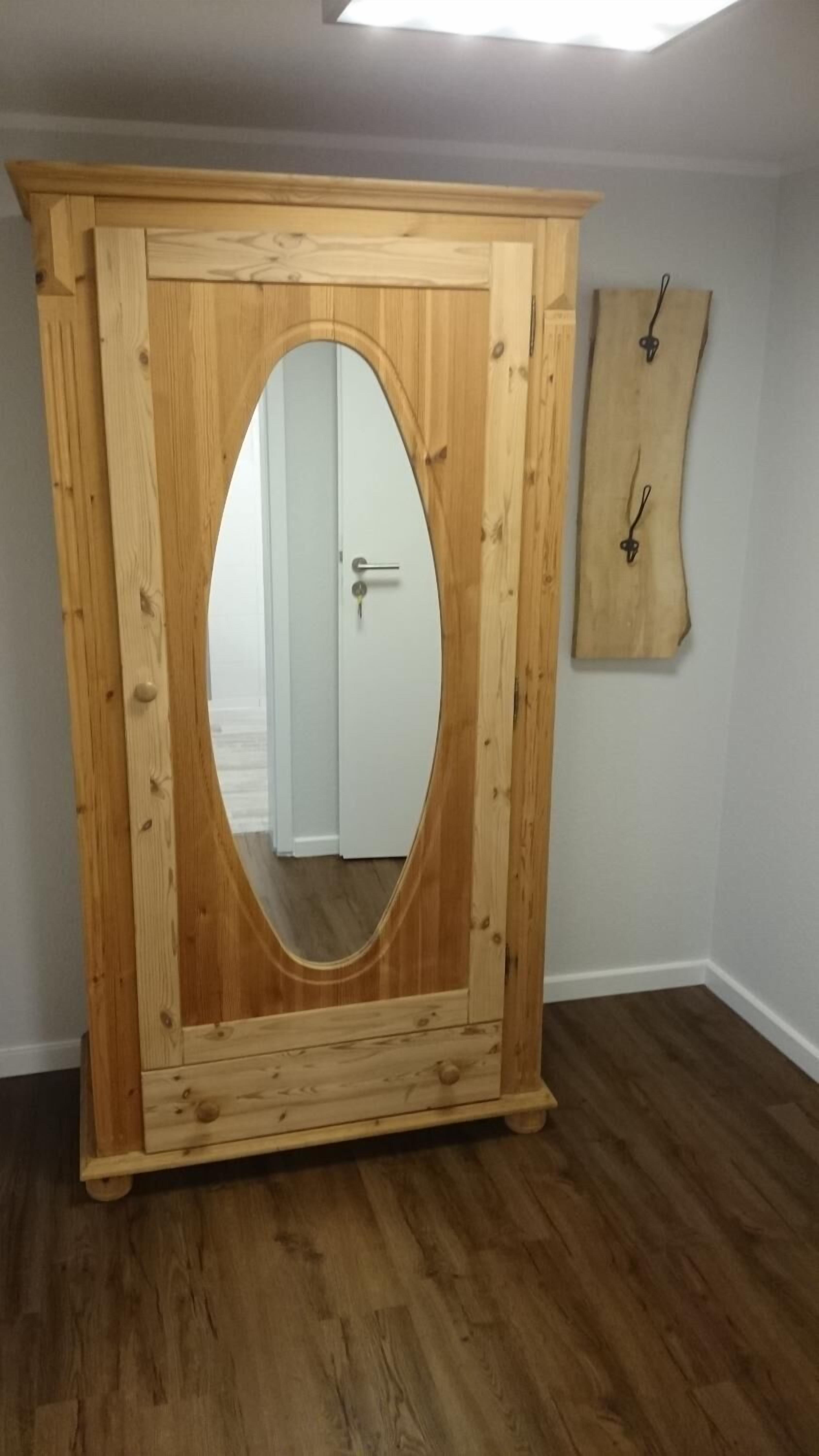 A wooden wardrobe with a large mirror and a door.