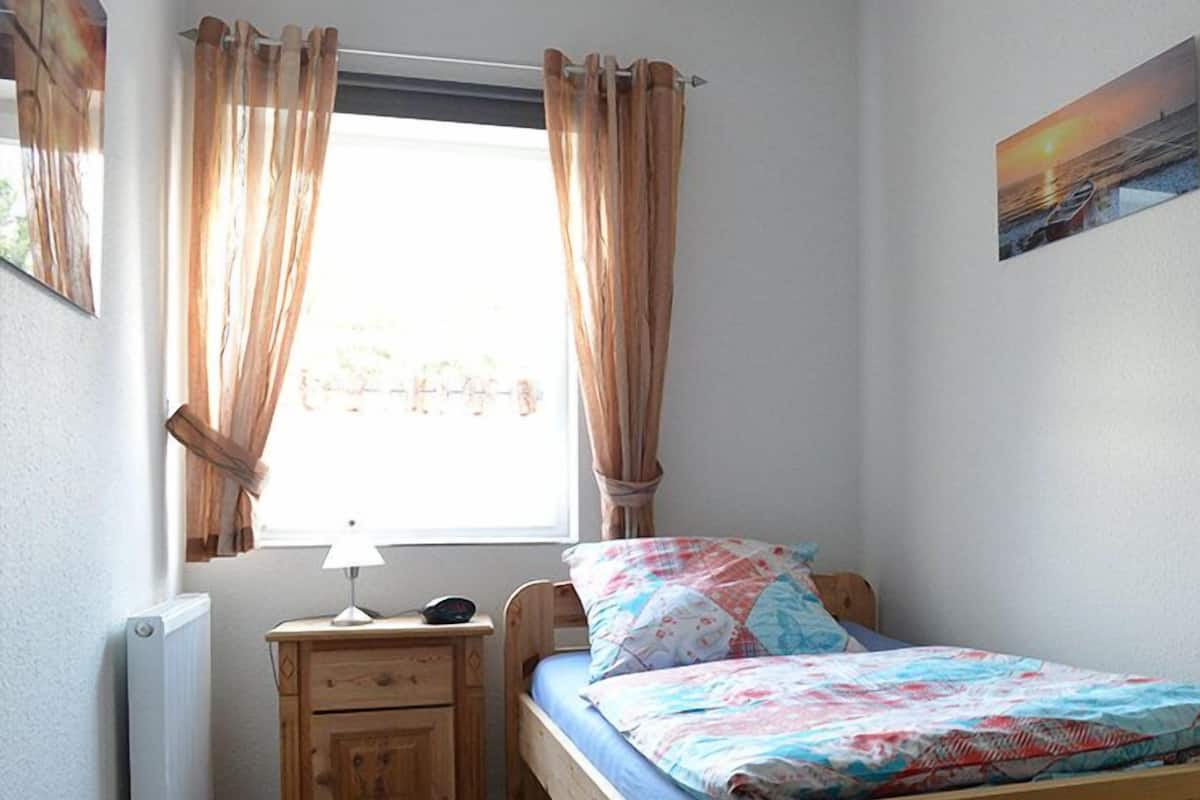 A bedroom with a wooden bed, a nightstand, a lamp, and a window with curtains.