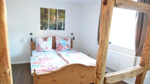 Un dormitorio con cama de madera, ventana con cortinas y radiador.