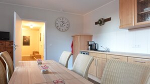 Un comedor con una mesa de madera, sillas, un reloj y una zona de cocina con armarios y electrodomésticos.