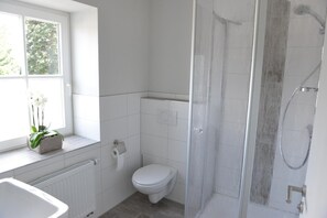 A bathroom with a toilet, a shower, and a window with a plant.