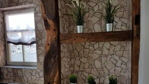 Una habitación con pared de piedra, vigas de madera y plantas en macetas sobre estantes.