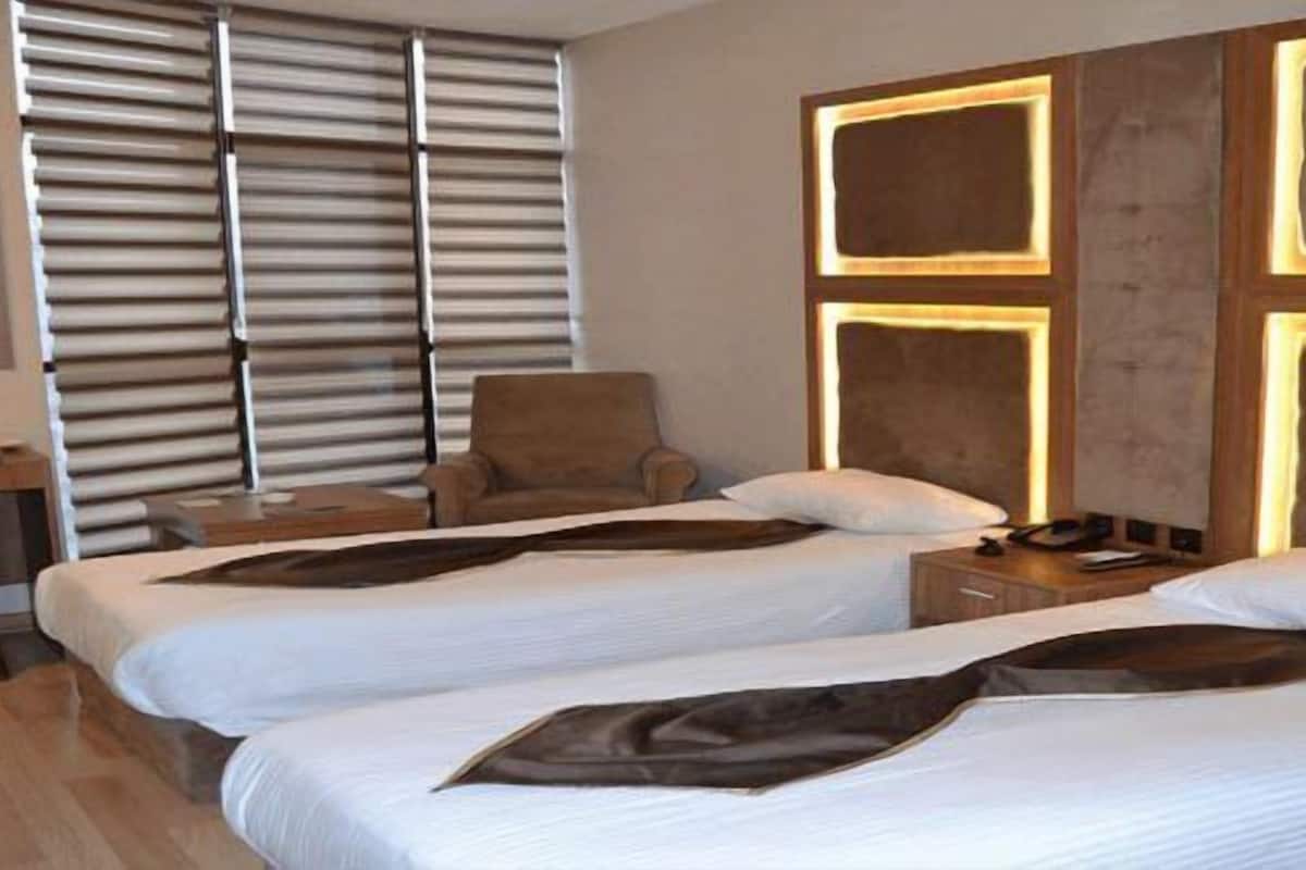 Ein Hotelzimmer mit zwei Betten, einem Sessel, einem Nachttisch und einem Fenster mit Jalousien.