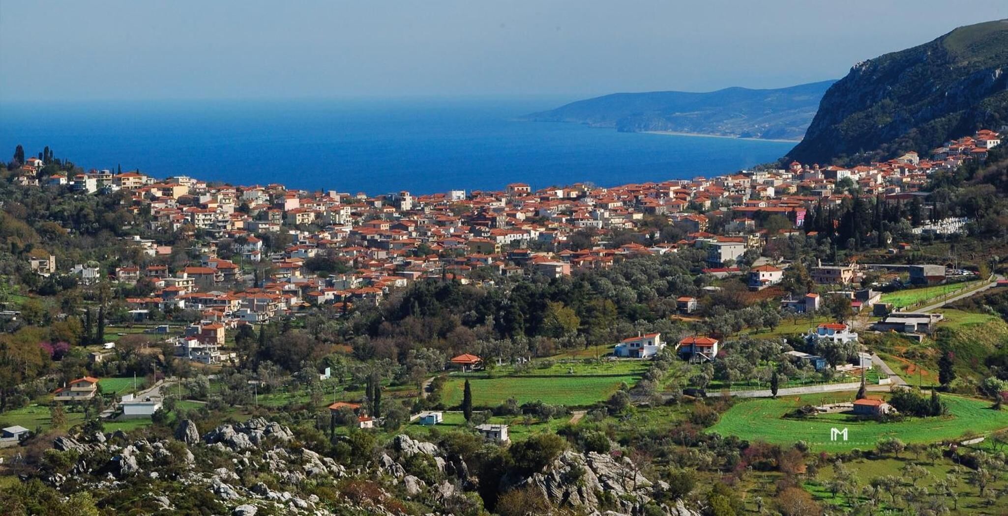 A coastal town with red-roofed buildings, green fields, and a view of the sea.