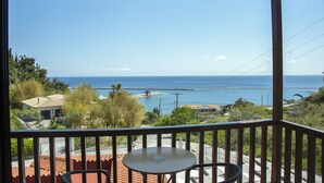 A balcony with a table and chairs overlooking a coastal view with houses and a clear sky. - Corali Hotel (Kymi-Aliveri)