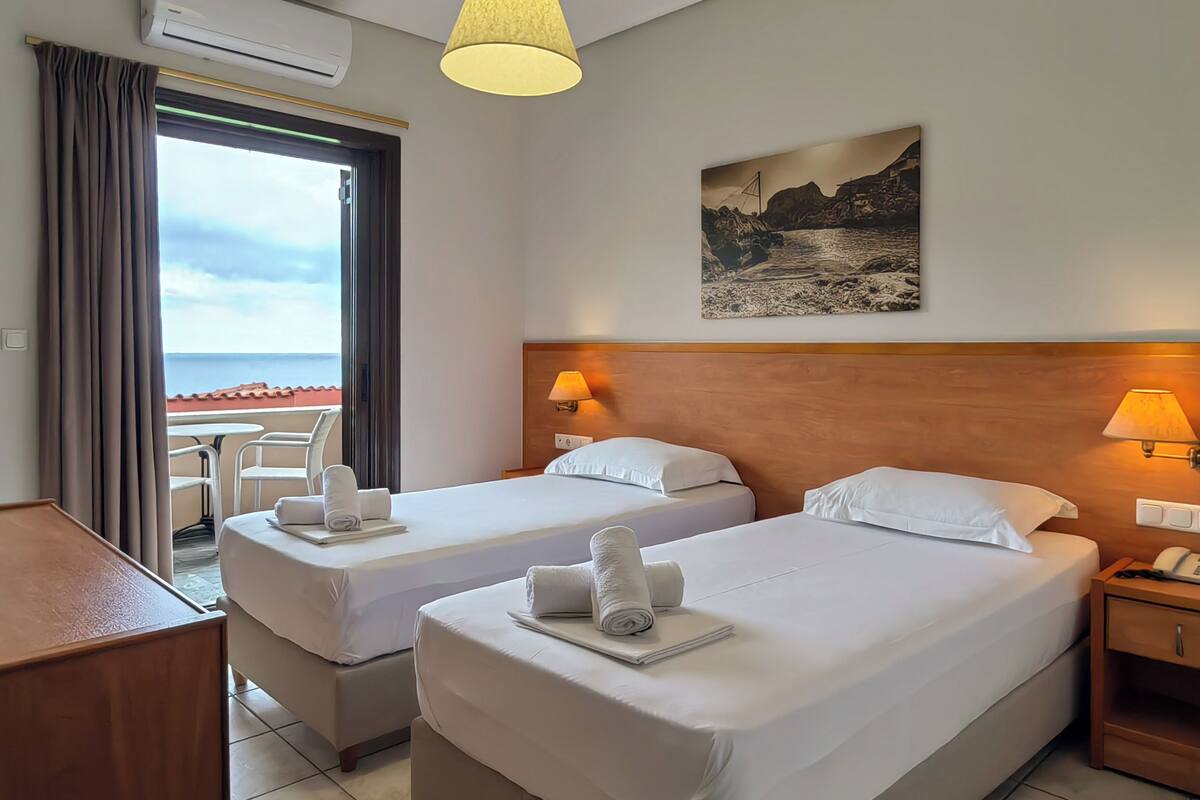 Een hotelkamer met twee bedden, een bureau, een stoel en uitzicht op zee.