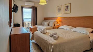 A hotel room with two beds, a TV, a desk, a lamp, and a view of the sea.