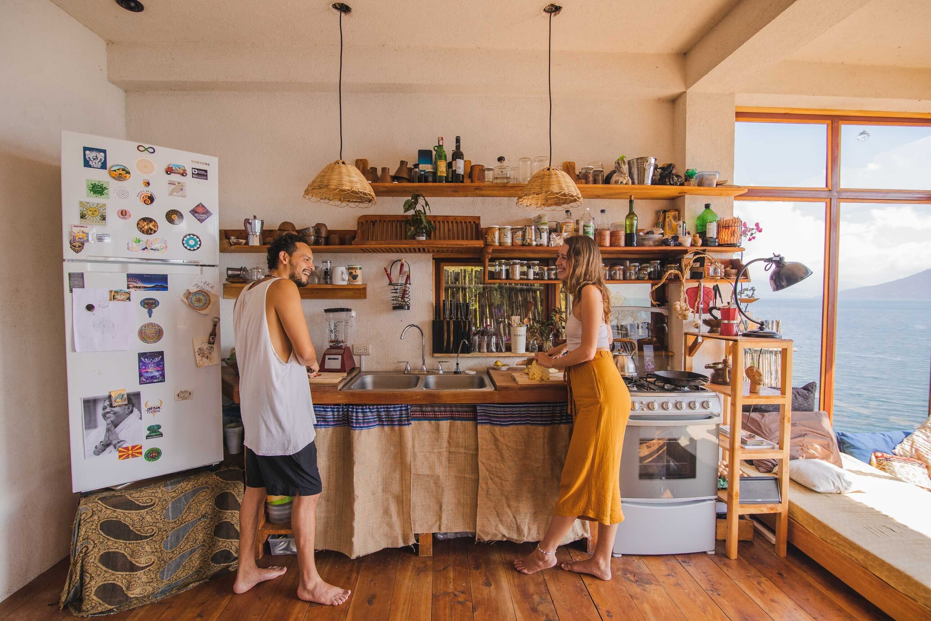 Una cocina con armarios de madera, estufa y refrigerador con imanes. Hay una ventana con vista al mar.