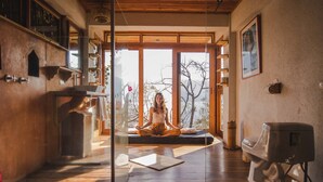 A room with a large window, a wooden floor, and a kitchen area with a coffee machine. - Baraka Atitlan - Lake & Beach (San Marcos La Laguna)