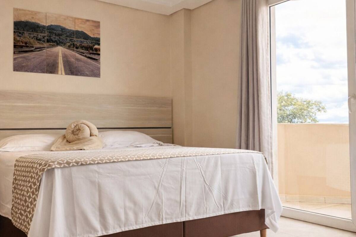 Un dormitorio con cama, un cuadro en la pared y vistas a través de una ventana.