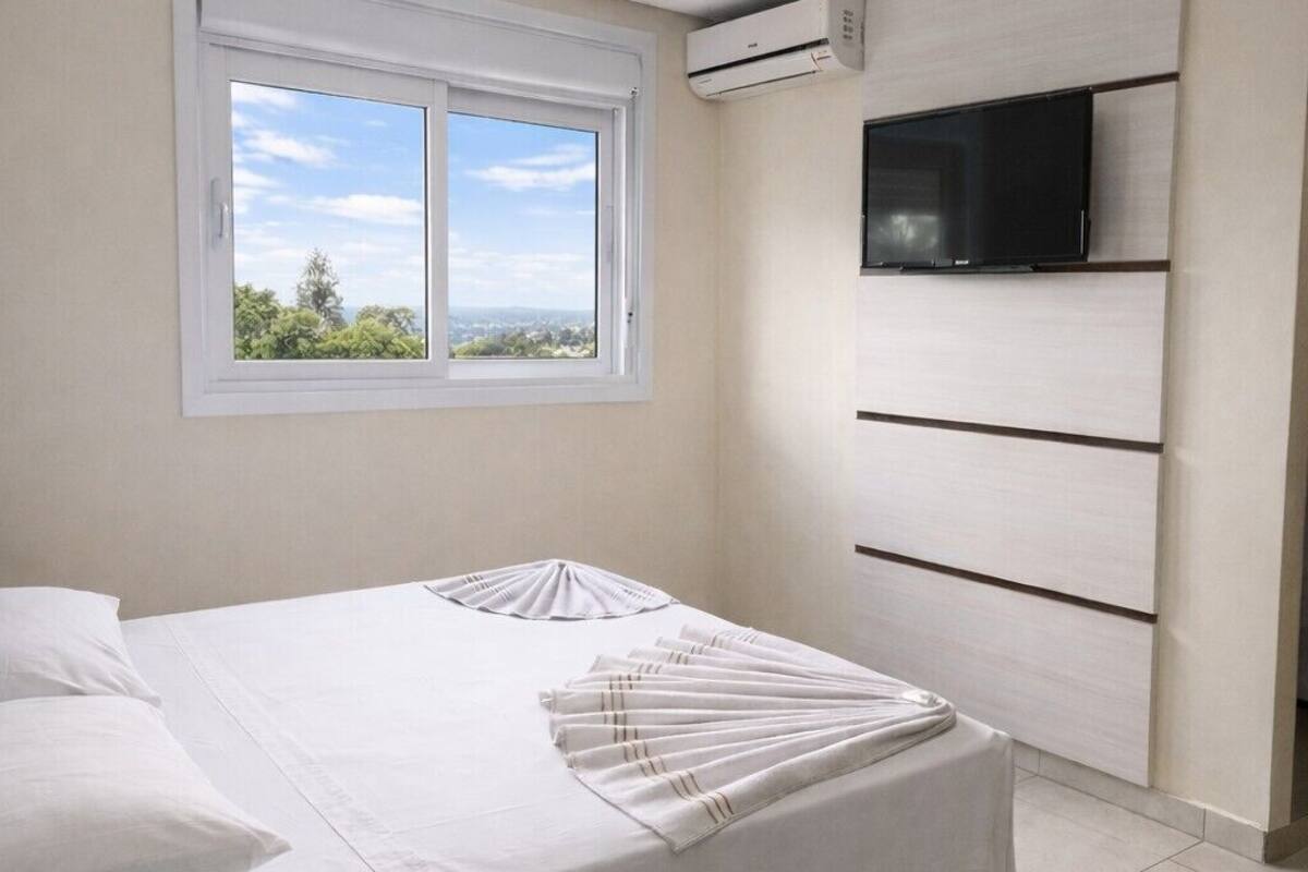 Un dormitorio con cama, ventana, equipo de aire acondicionado y televisor montado.