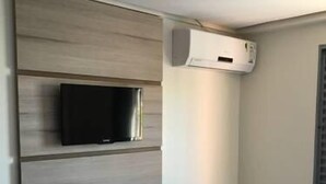 Une pièce dotée d’une étagère intégrée pour la télévision, d’un appareil de climatisation et d’une fenêtre avec des stores.