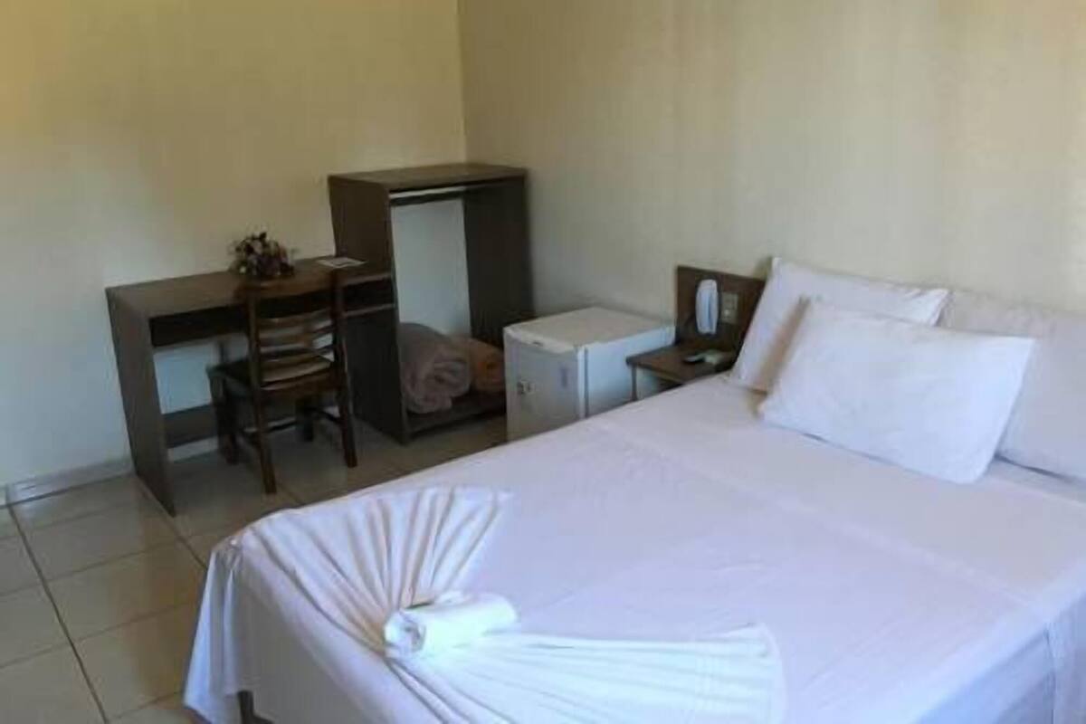 Una habitación de hotel con cama, escritorio, silla, armario y mesita de noche.