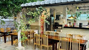 An outdoor dining area with wooden tables and chairs, surrounded by greenery and a brick wall. - RungNara Pool Villa (San Sai)