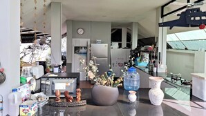 A modern kitchen with a refrigerator, stove, and various kitchen utensils. There is a dining area with a table and chairs, and a large window offering a view of the outdoors. - RungNara Pool Villa (San Sai)