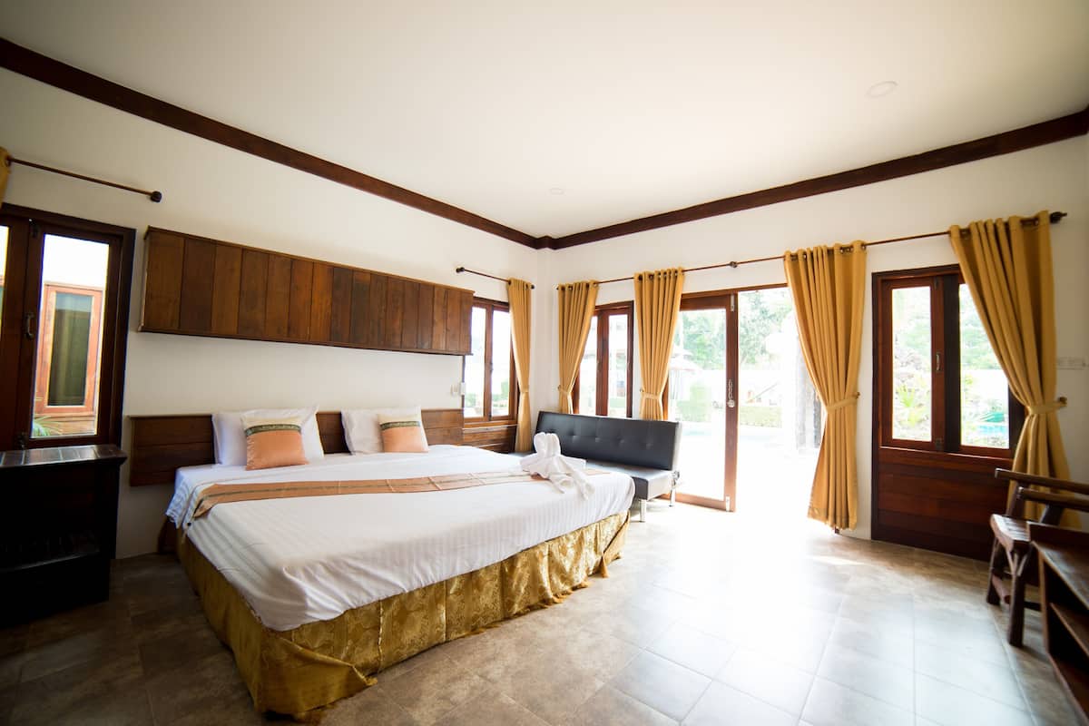 A spacious bedroom with a large bed, wooden headboard, and a bench by the window.