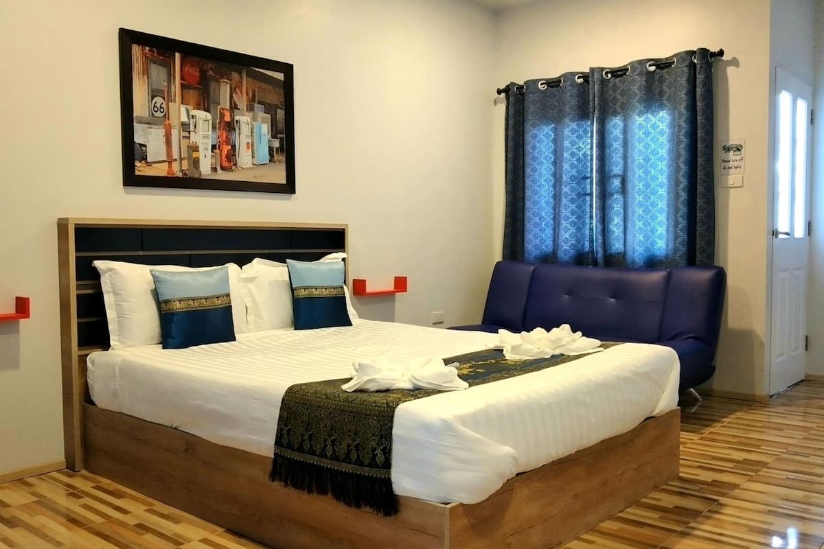A hotel room with a large bed, a headboard, a blue chair, a painting on the wall, and a window with curtains.