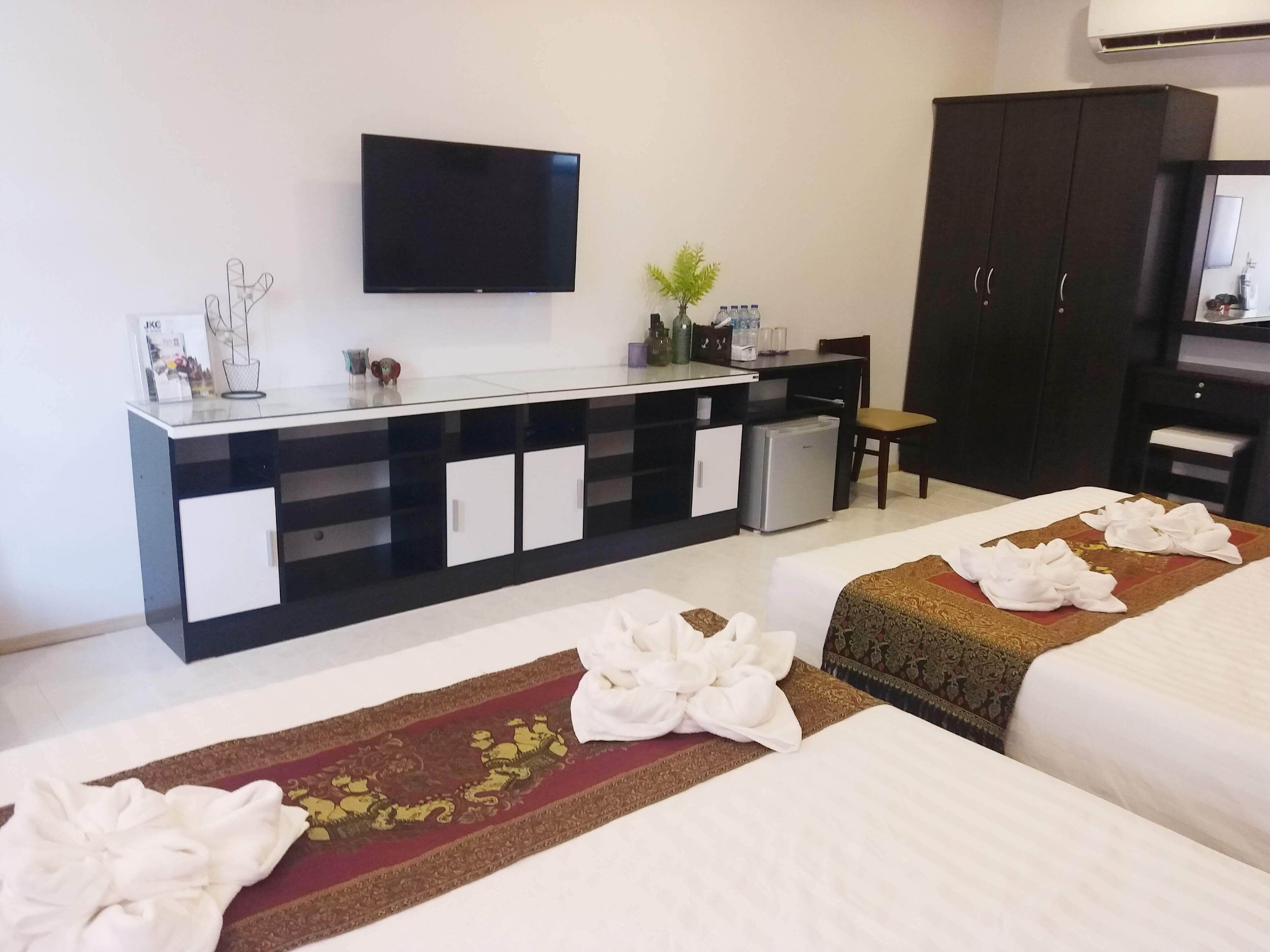 Habitación de hotel con dos camas, un televisor montado en la pared, un escritorio pequeño con refrigerador y un armario oscuro.