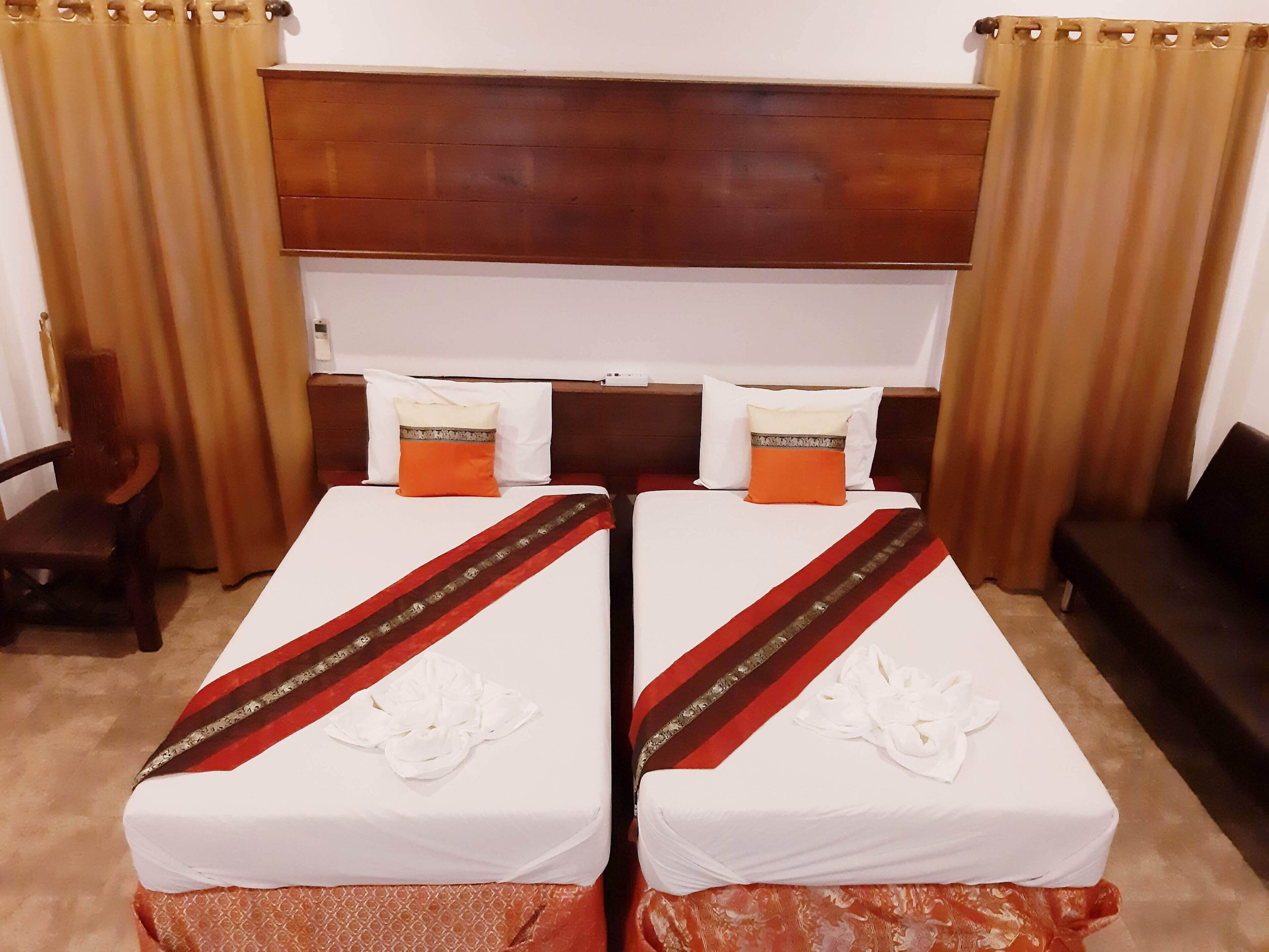 Habitación de hotel con dos camas individuales, un cabecero de madera, una pequeña silla de madera y un sofá de color oscuro.