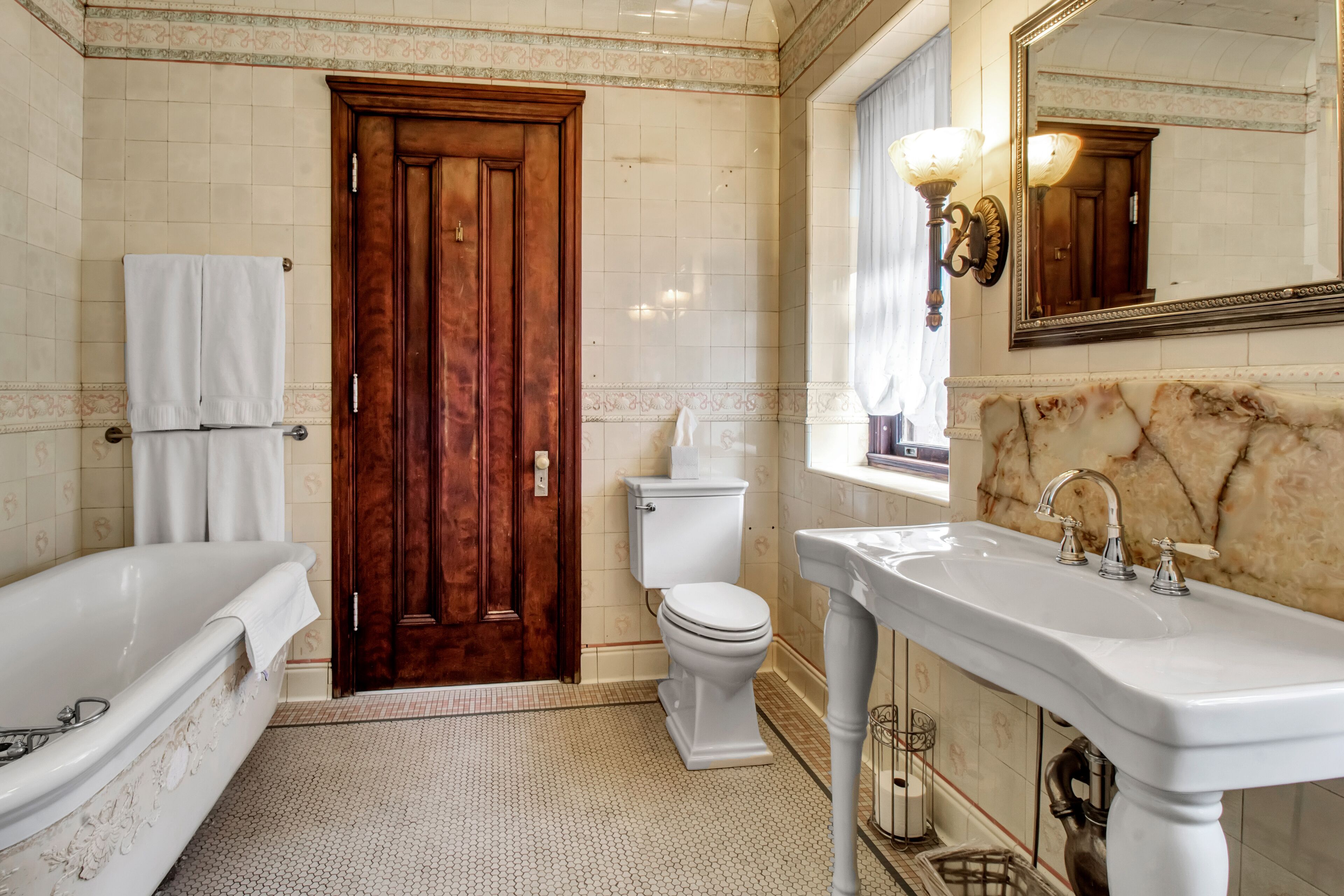 Ein Badezimmer mit Holztür, Toilette in Weiß und einem großen Waschbecken mit Marmorplatte.