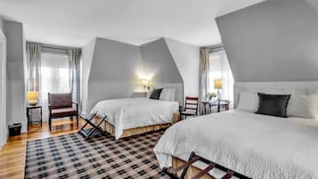 Ein Hotelzimmer mit zwei Betten, einem Schachbrettteppich, einem Holzstuhl, einem kleinen Tisch mit Lampe und einem Fenster mit Vorhängen.