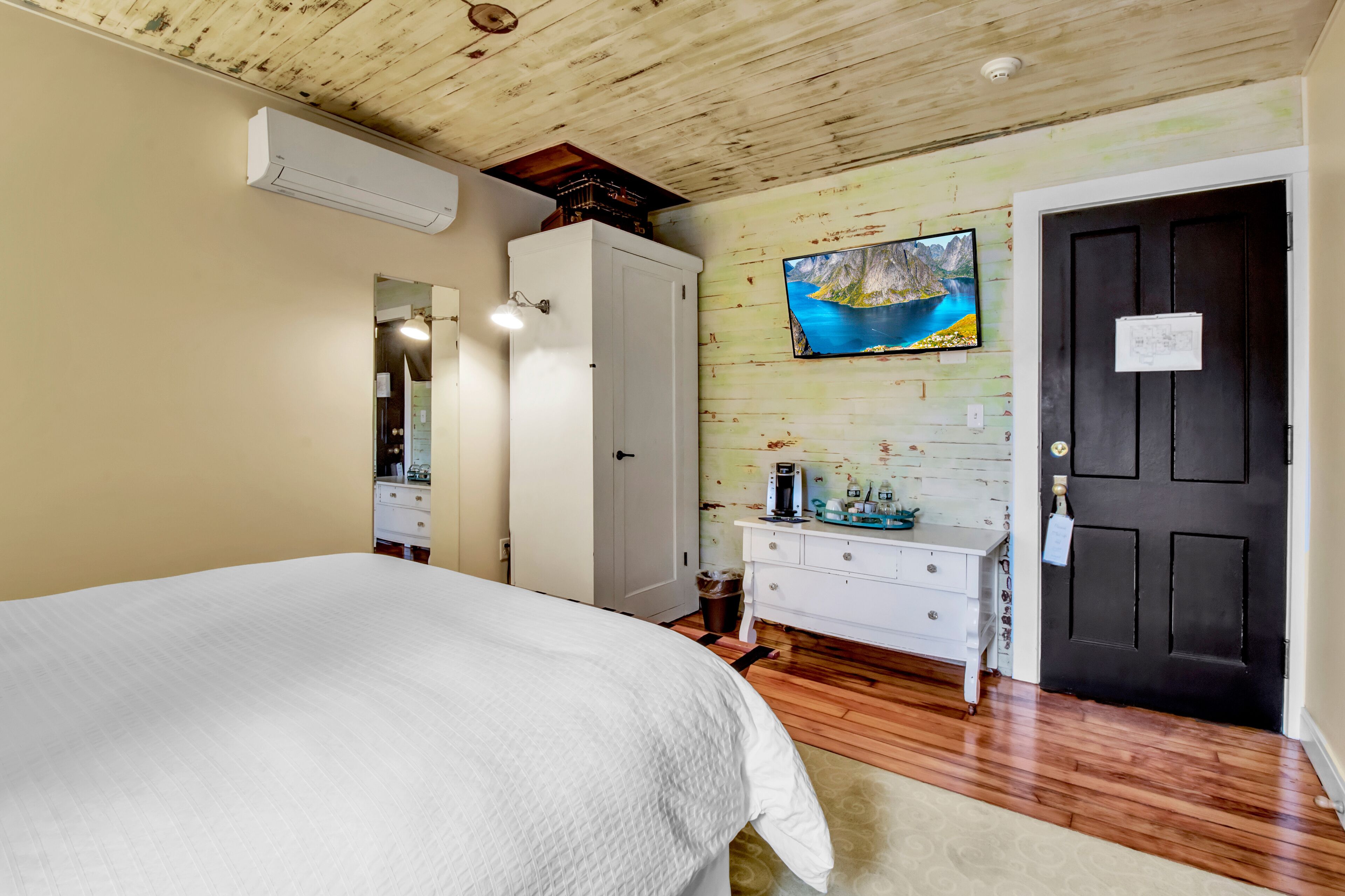Ein Schlafzimmer mit einem Bett, einem Schminktisch, einem Spiegel, einer Klimaanlage und einem Bild von einem See an der Wand.