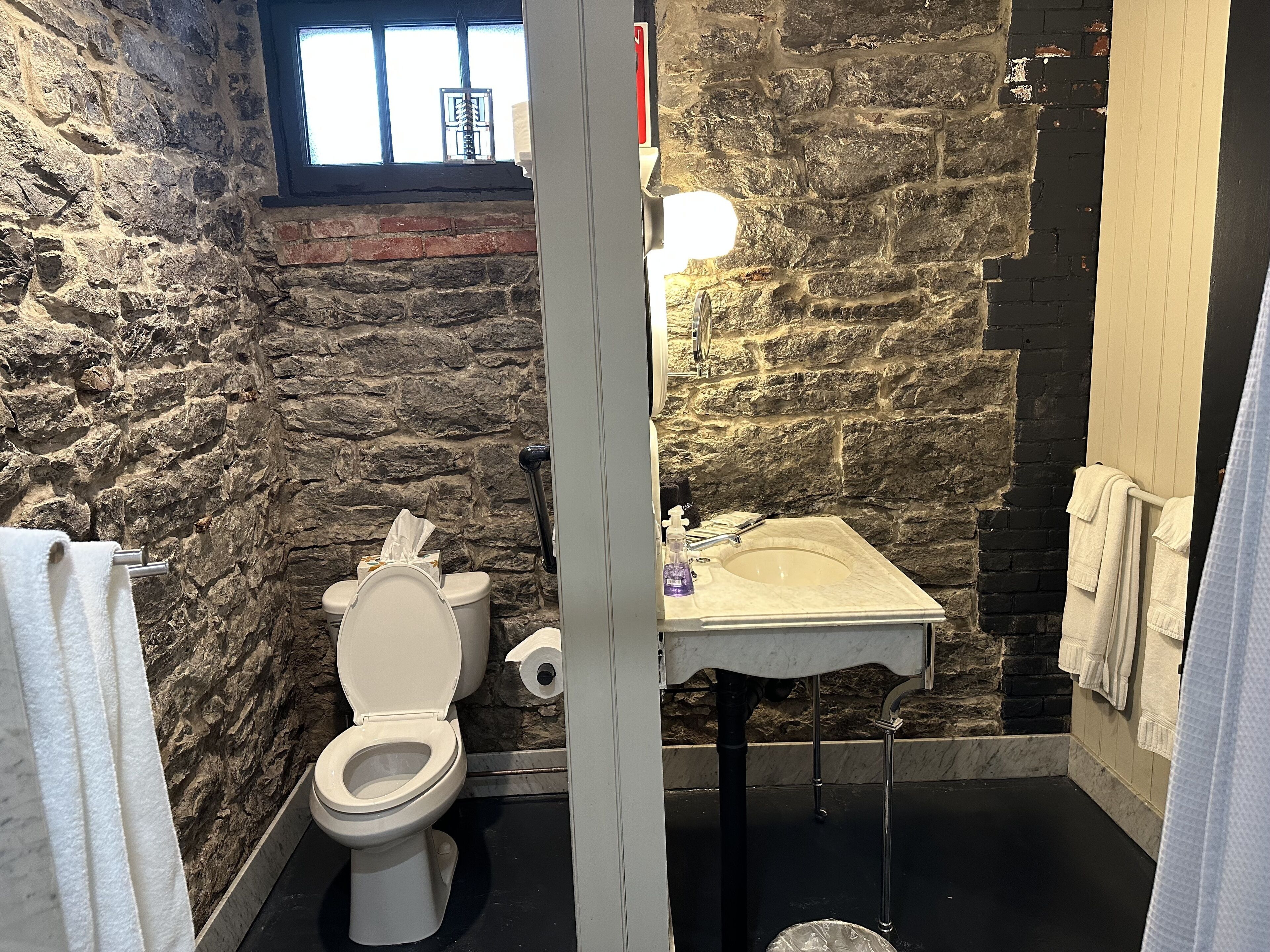 Un bagno con parete in pietra, un water, un lavandino e una finestra.