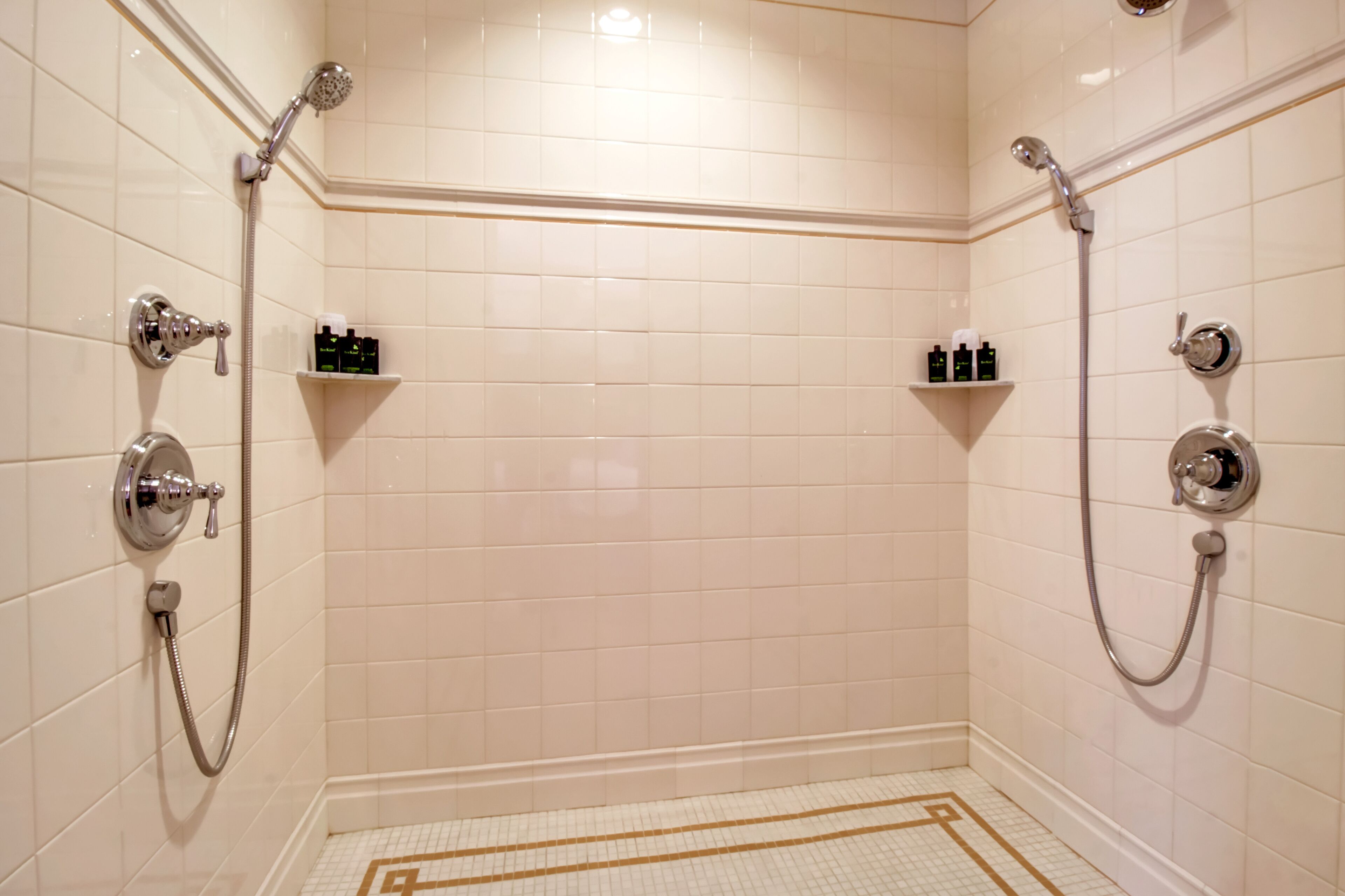 A bathroom with two showerheads, a tiled floor, and two shelves with toiletries.