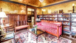 A room with a red patterned sofa, wooden bookshelves, a chandelier, and a traditional wooden coffee table. - InnBuffalo off Elmwood (Buffalo)