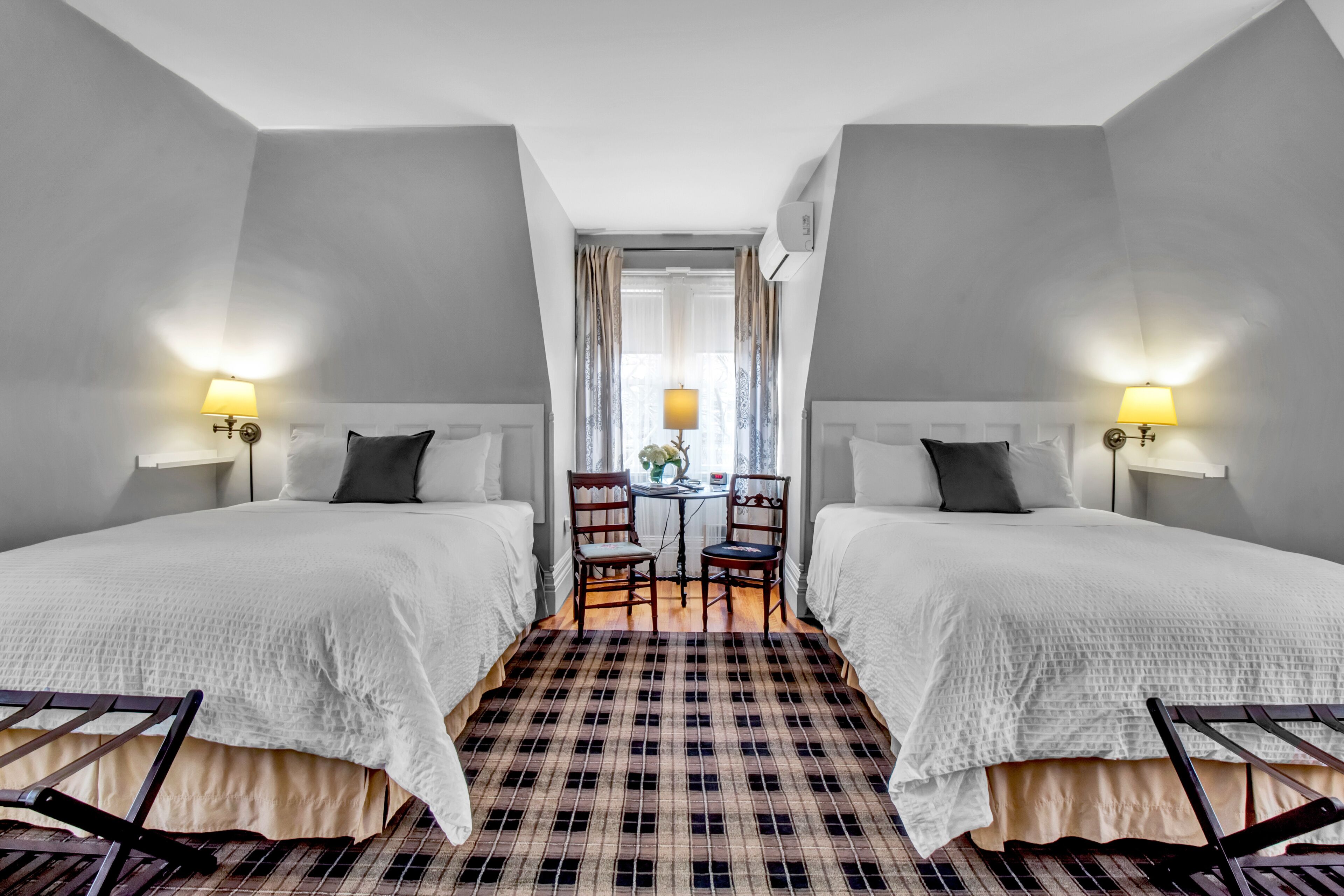 A hotel room with two beds, a checkered floor, a small table with chairs, and lamps on either side of the bed.