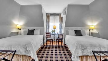 A hotel room with two beds, a checkered floor, a small table with chairs, and lamps on either side of the bed.