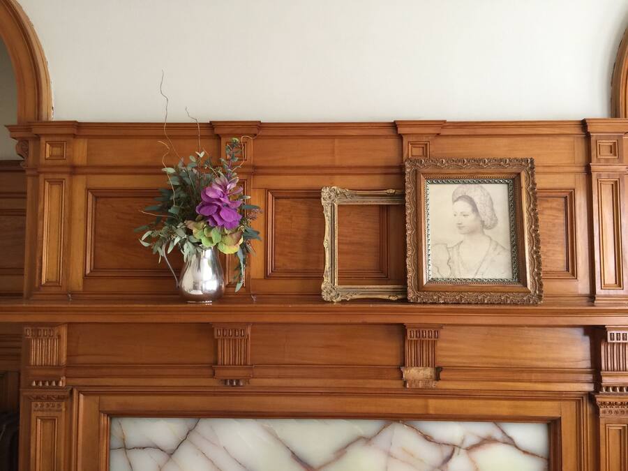 A wooden mantelpiece with a vase of flowers and a framed picture.