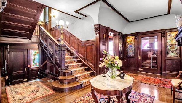 A grand staircase with ornate woodwork and a chandelier, leading to a room with a large wooden door and a stained glass window. - InnBuffalo off Elmwood (Buffalo)
