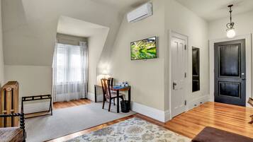 A room with a wooden floor, a desk with a chair, a lamp, a TV on the wall, and a door.