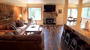 A cozy living room with a stone fireplace, a large TV, and a wooden ceiling. - 113 Standard Condo (Mammoth Lakes)