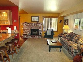 A living room with a fireplace, a sofa, a coffee table, and a bar area with stools.