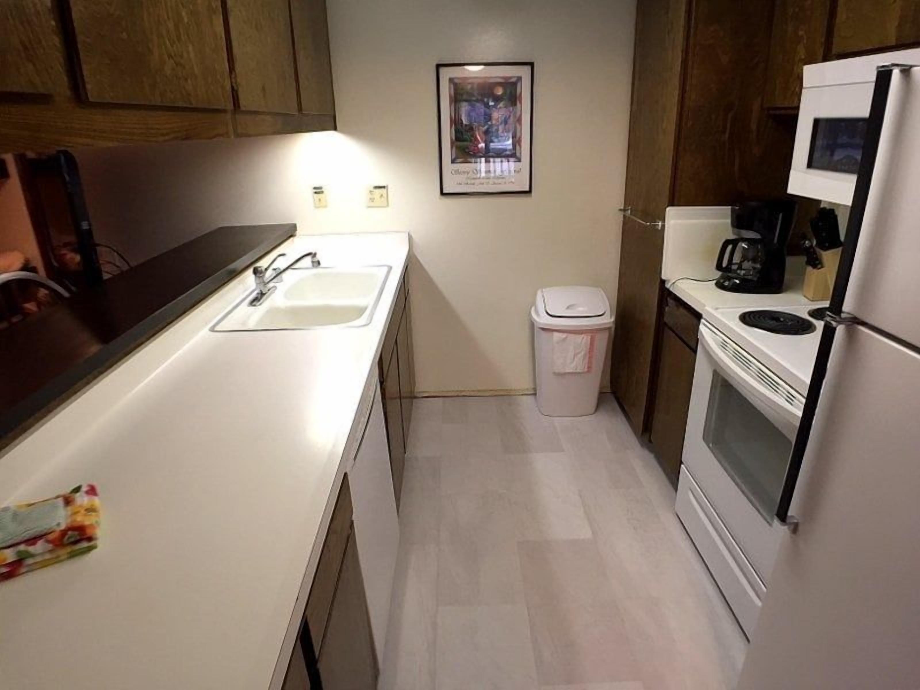 A compact kitchen with a sink, a trash bin, a refrigerator, and a microwave.