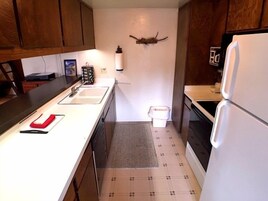 A compact kitchen with wooden cabinets, a white countertop, a sink, a stove, and a refrigerator.
