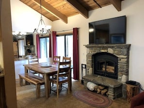 A cozy living room with a stone fireplace, wooden dining table, and chairs.