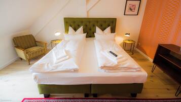 A double bed with a green upholstered headboard, two bedside lamps, a chair, and a framed picture on the wall.