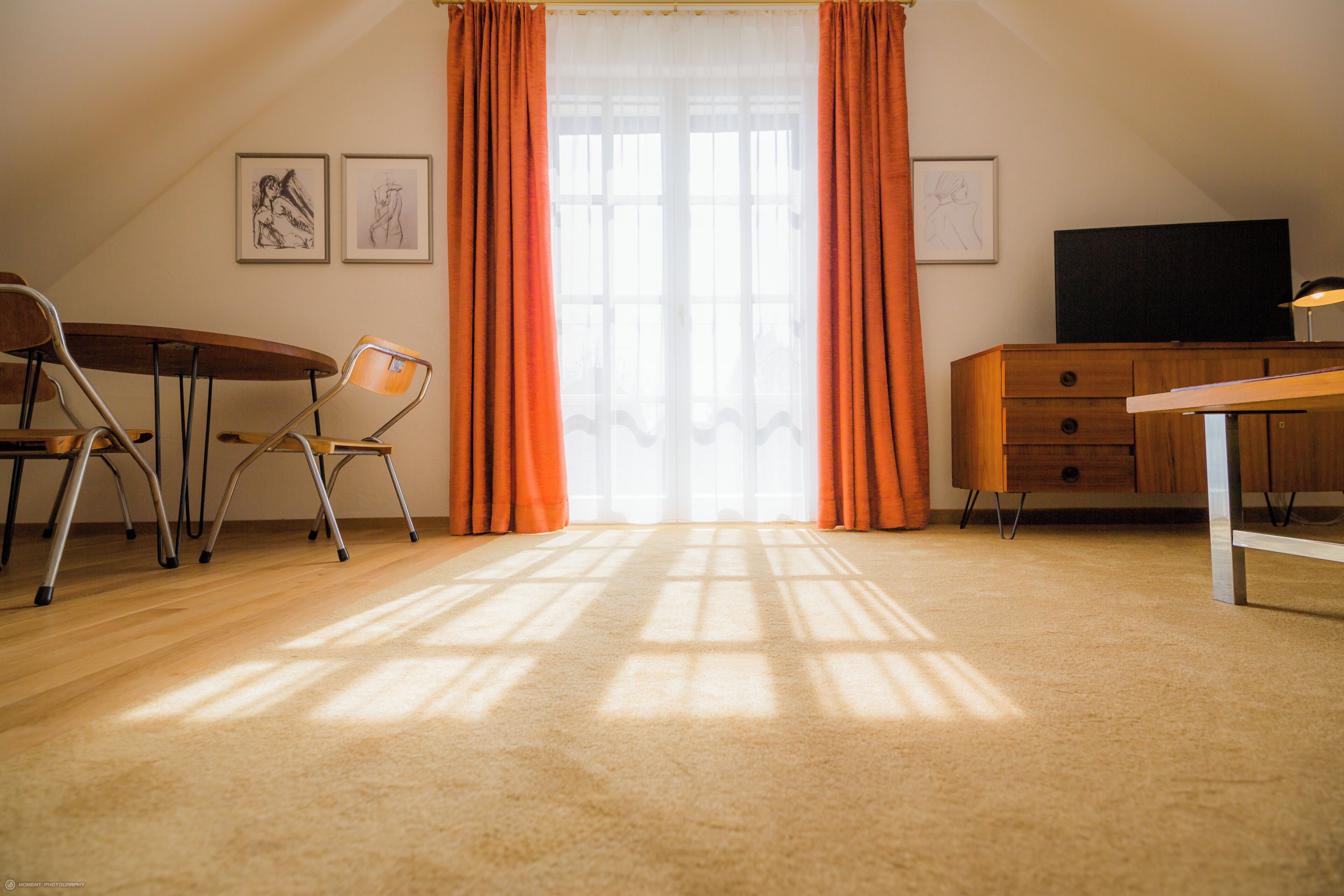 Una habitación con escritorio de madera, una silla, televisor y ventana con cortinas.