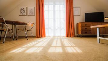 Una habitación con escritorio de madera, una silla, televisor y ventana con cortinas.