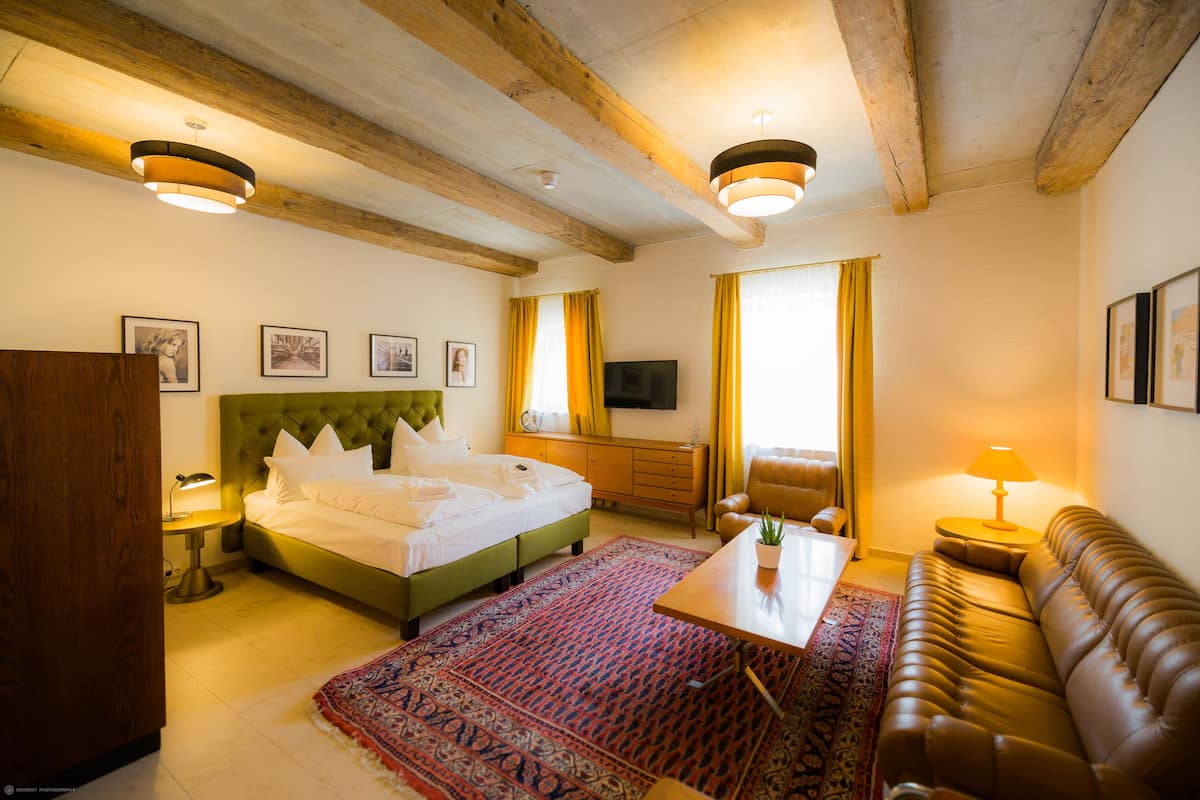 Habitación de hotel con cama, sofá, mesa de centro, televisor y techo de madera.